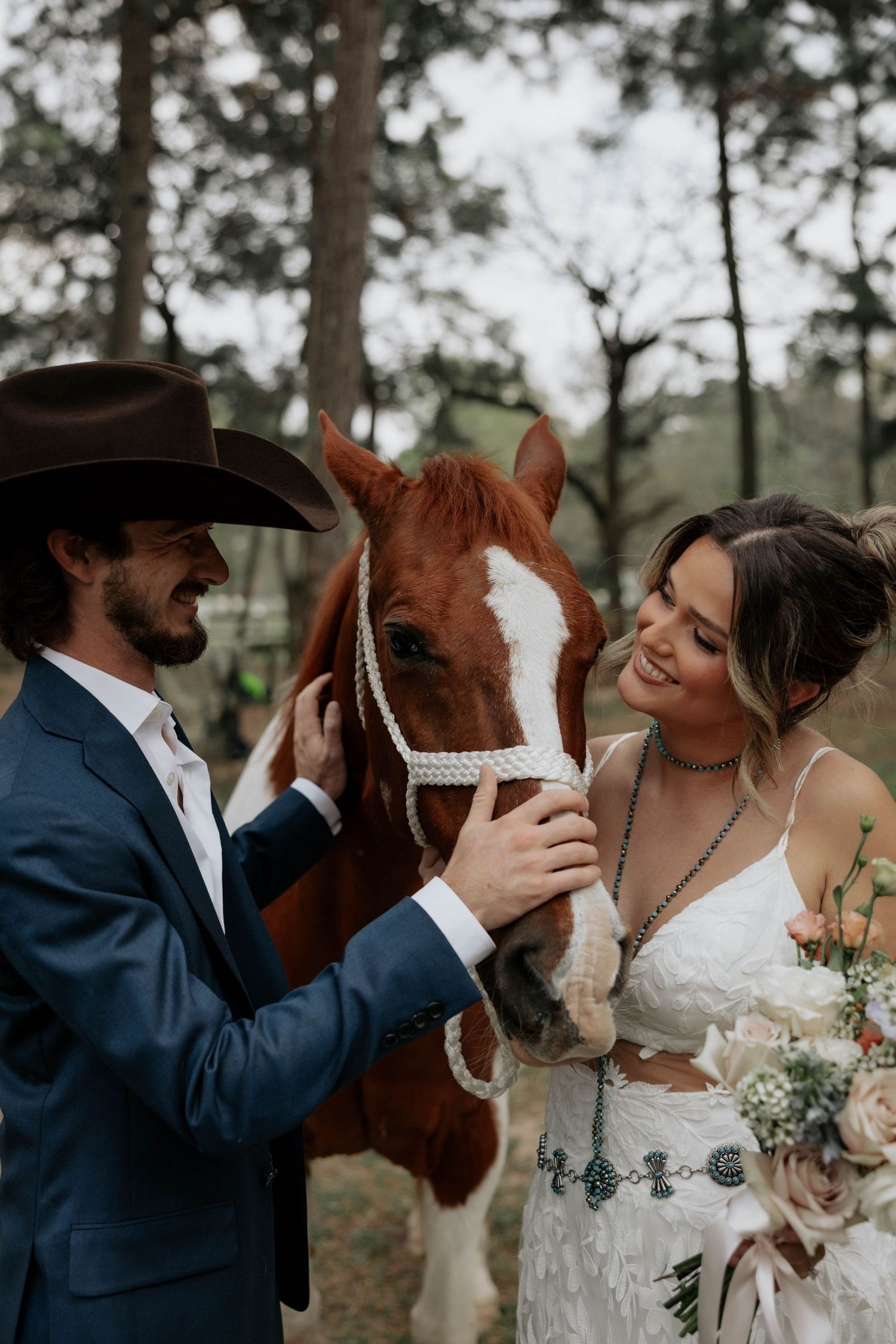 A newlywed couple shares tender moments with their beautiful chestnut horse during an outdoor wedding photoshoot in a pine forest.