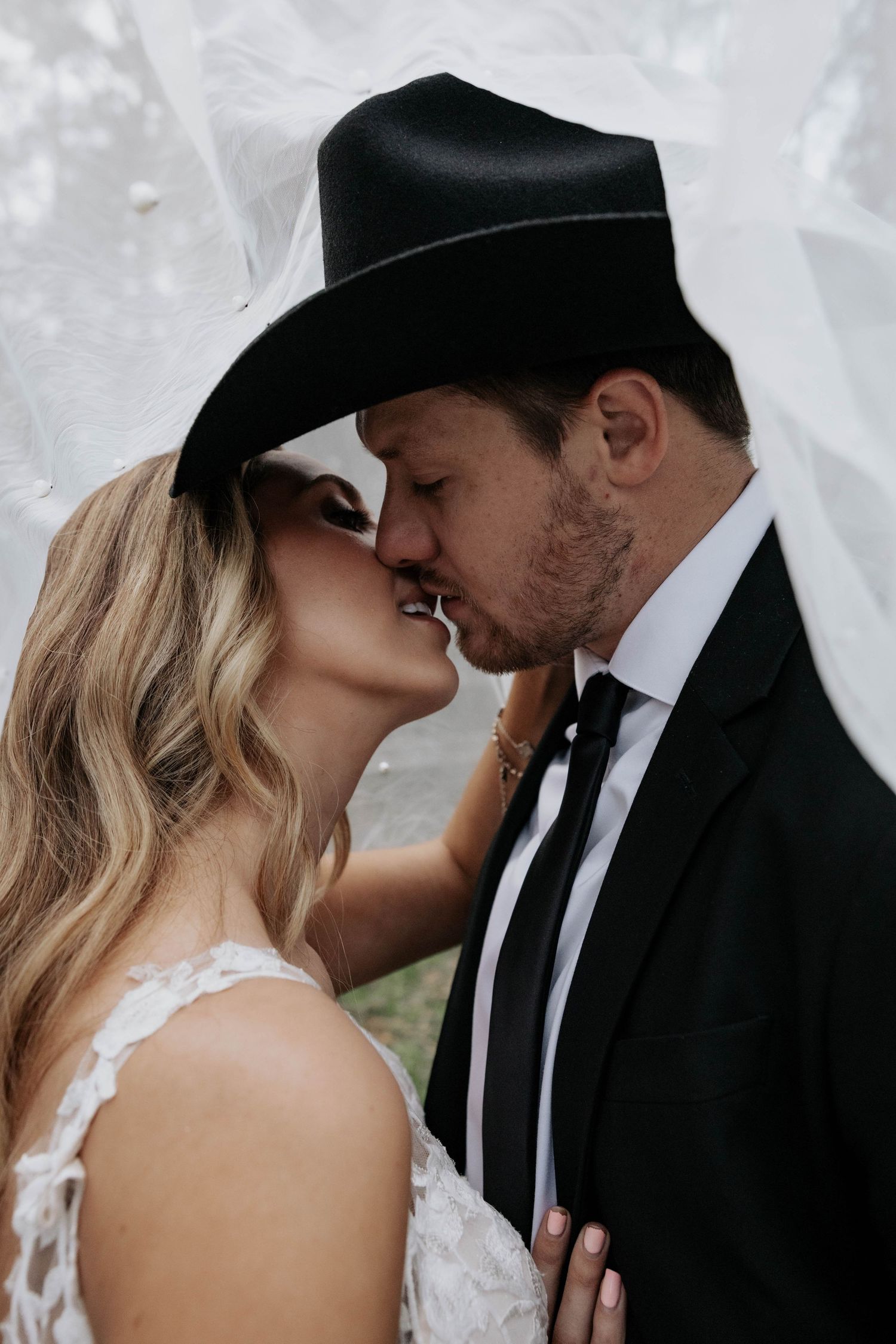 A romantic sequence of wedding photos showing a tender kiss between the bride in white lace and groom in black suit and hat.
