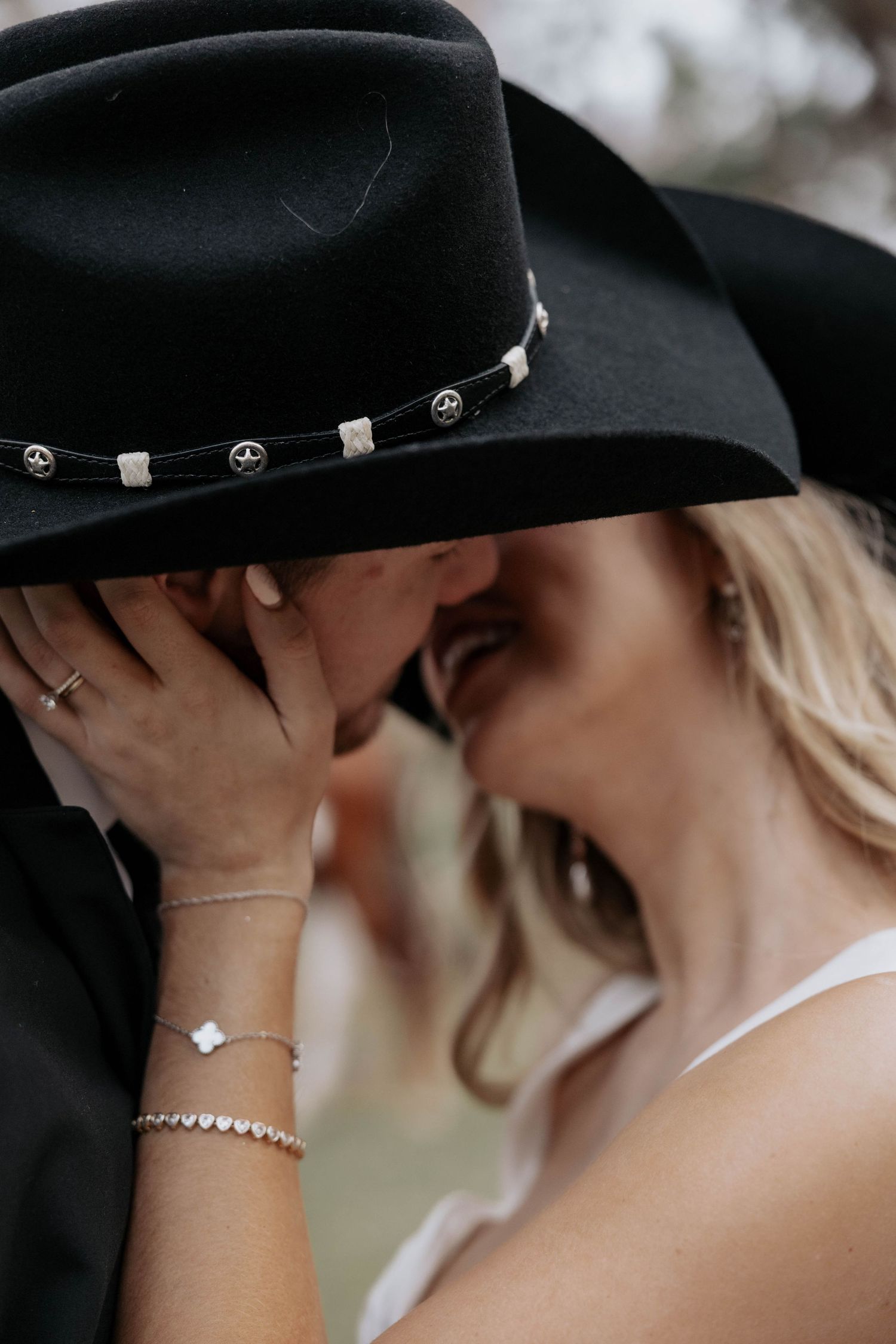 Close up of a couple sharing an intimate moment with one wearing a black cowboy hat decorated with silver studs.