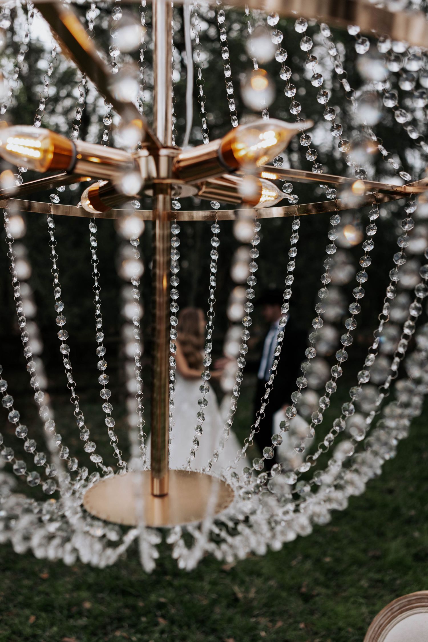 Close-up detail of an elegant crystal chandelier with cascading glass beads and copper fixtures against a dark background.