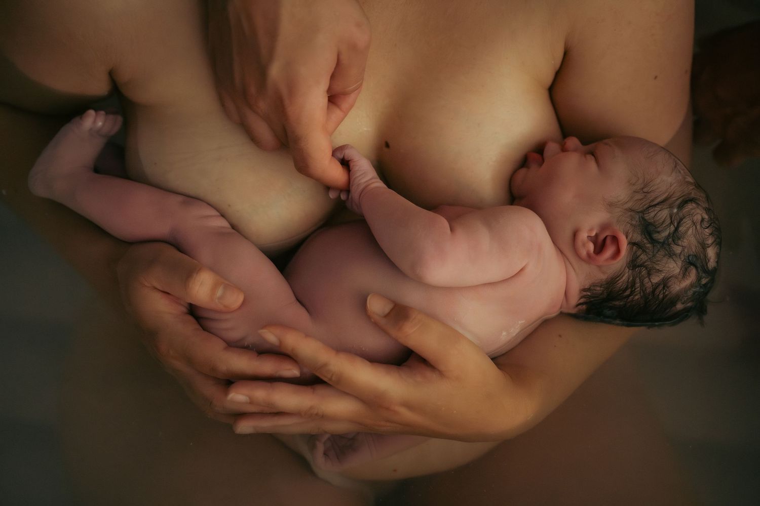 close-up van een baby die in bad is geboren en bij haar moeder op de borst ligt en met haar kleine handje papa stevig vasthoudt