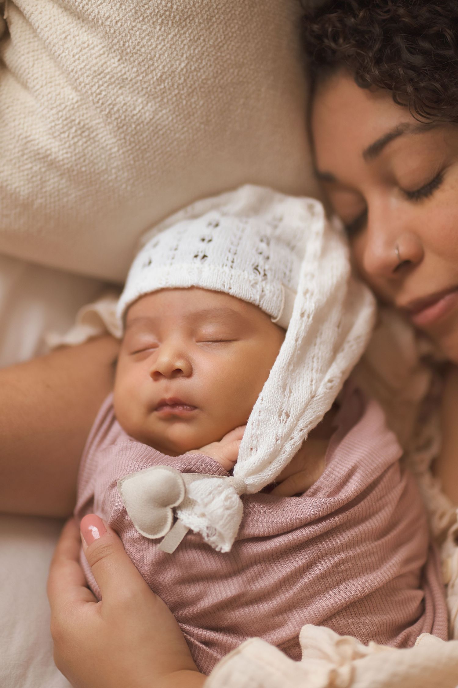 Sleeping baby in pink wearing white bonnet nestles close in peaceful moment.