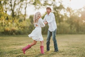 Couple in white outfits share romantic moments in a sunlit meadow during golden hour photo session.