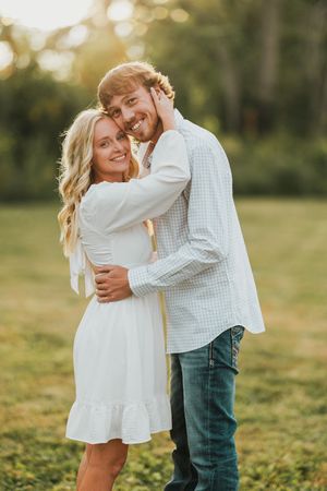 A couple embraces in a sunny outdoor field during a romantic photoshoot session.