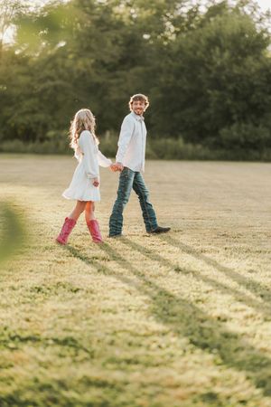 Children's feet walking together in a grassy field at sunset casting long shadows.