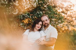 A romantic couple embraces in a sun-drenched outdoor setting with golden autumn foliage in the background.