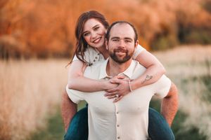 A couple shares a joyful embrace in a field with warm autumn tones in the background during golden hour.