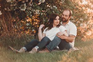 A couple sits together on the grass at sunset in a romantic outdoor setting with soft golden lighting.