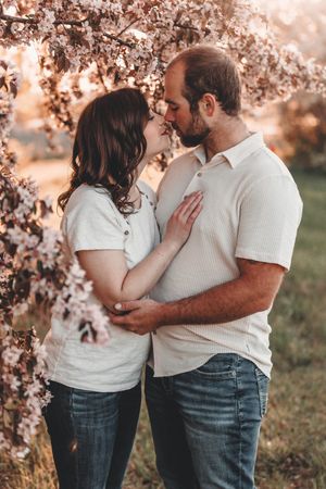 Two people in white shirts share a romantic moment among blooming spring cherry blossoms at sunset.