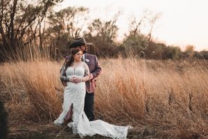 Couple embraces romantically in a golden field at sunset, bride wearing flowing white lace gown.