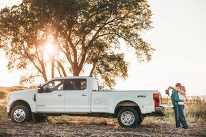 A white Ford Super Duty pickup truck parked near a large tree at sunset with silhouettes in the background.