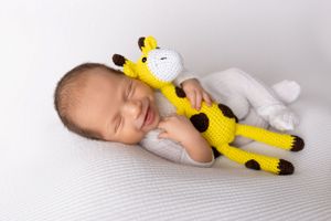 Sleeping baby lying on white blanket cuddling with yellow knitted giraffe plush toy in Newton, NJ - Newborn Photographer