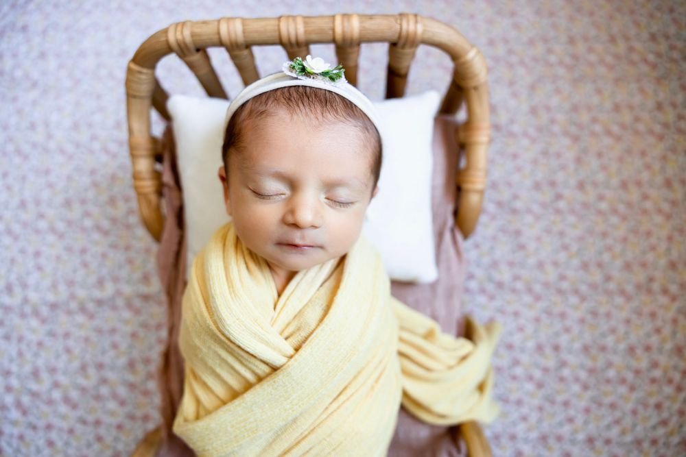 Newborn baby swaddled in yellow wrap sleeping peacefully in a small wicker bassinet with a white pillow. Newborn photographer in NJ