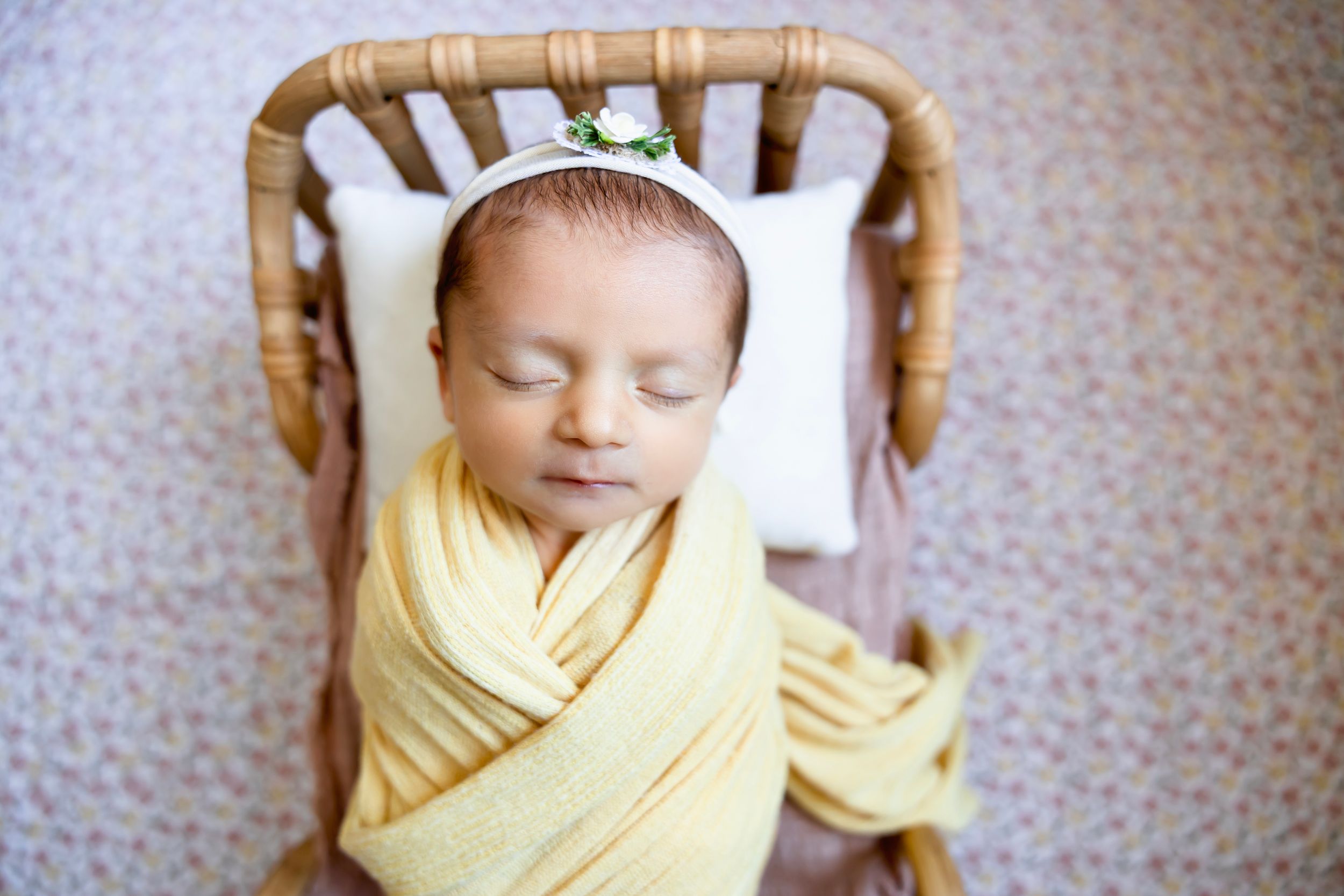 Newborn baby swaddled in yellow wrap sleeping peacefully in a small wicker bassinet with a white pillow. Newborn photographer in NJ