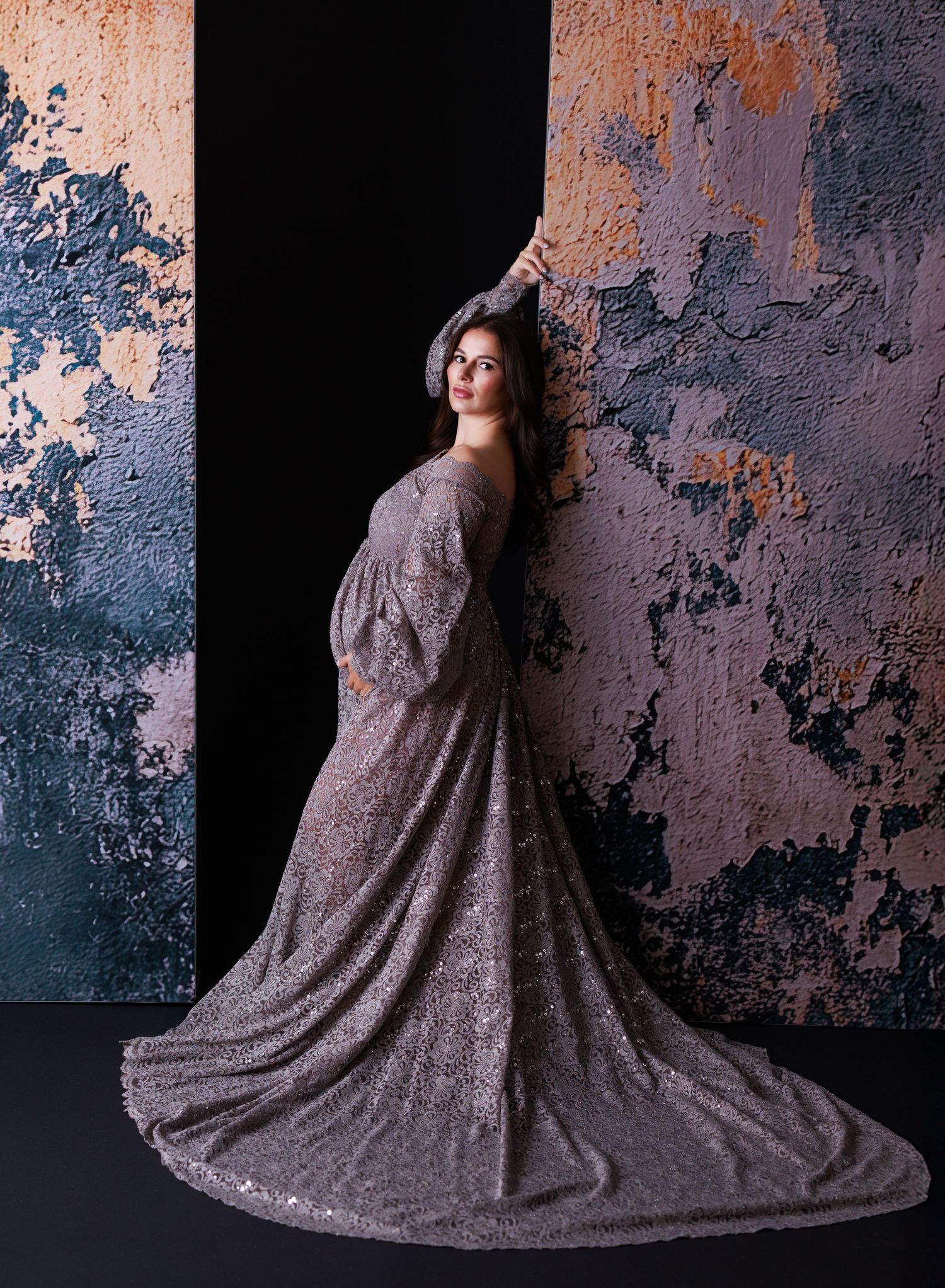A flowing gray sequined gown with long train photographed in dramatic poses against a textured copper wall.