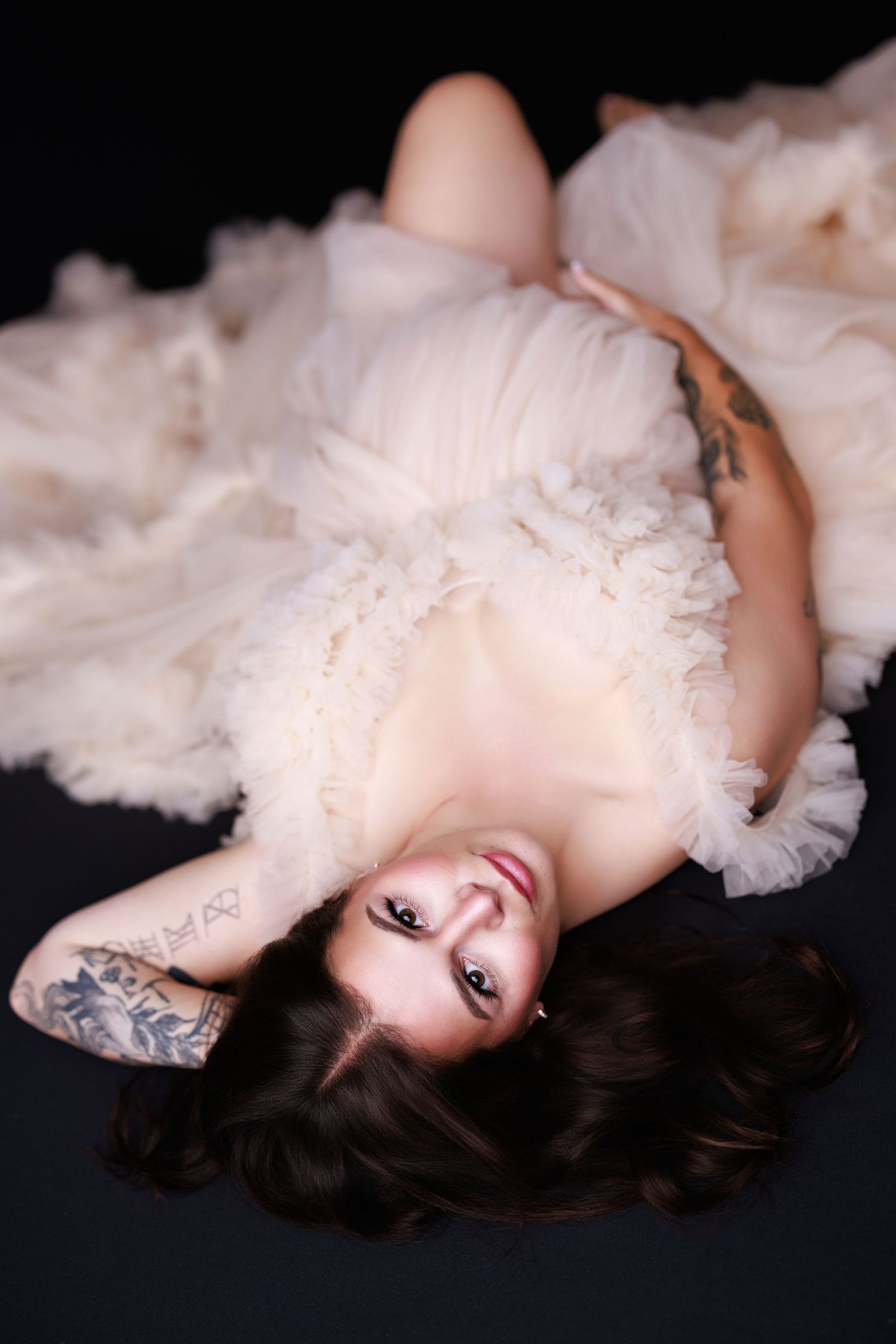 A model lies on a black surface wearing a white tulle dress in a dreamy boudoir photoshoot series.