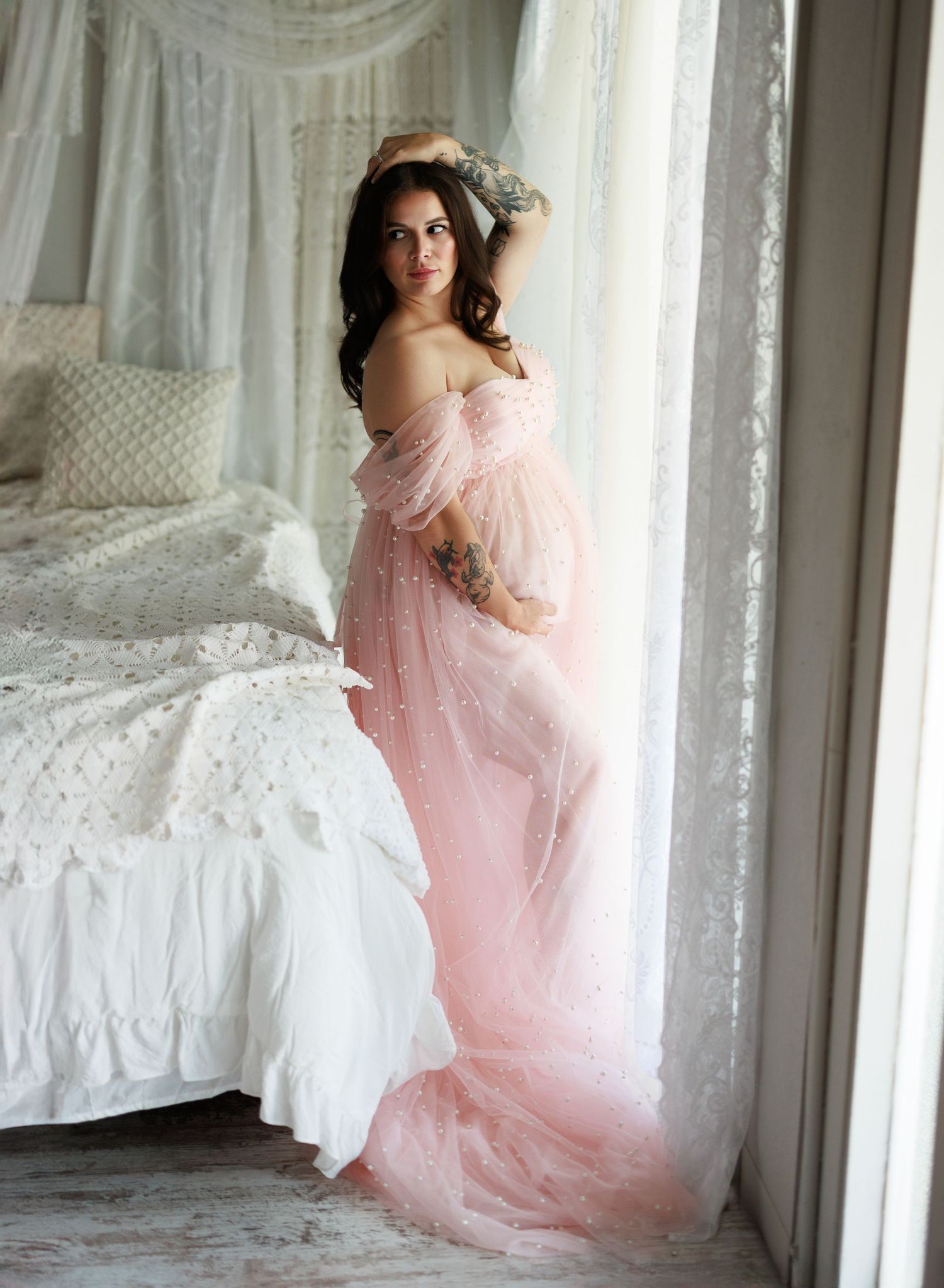 A dreamy boudoir photoshoot features soft pink tulle dresses and elegant white bedding in a bright sunlit room.