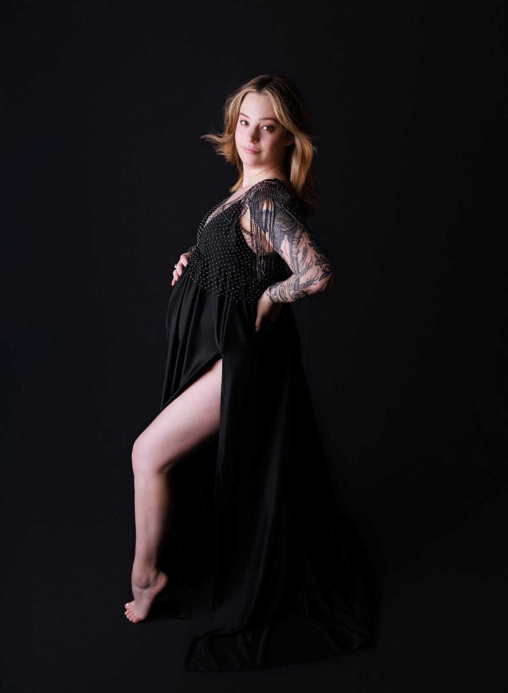 Dramatic maternity portrait of woman in black lace dress against dark background.
