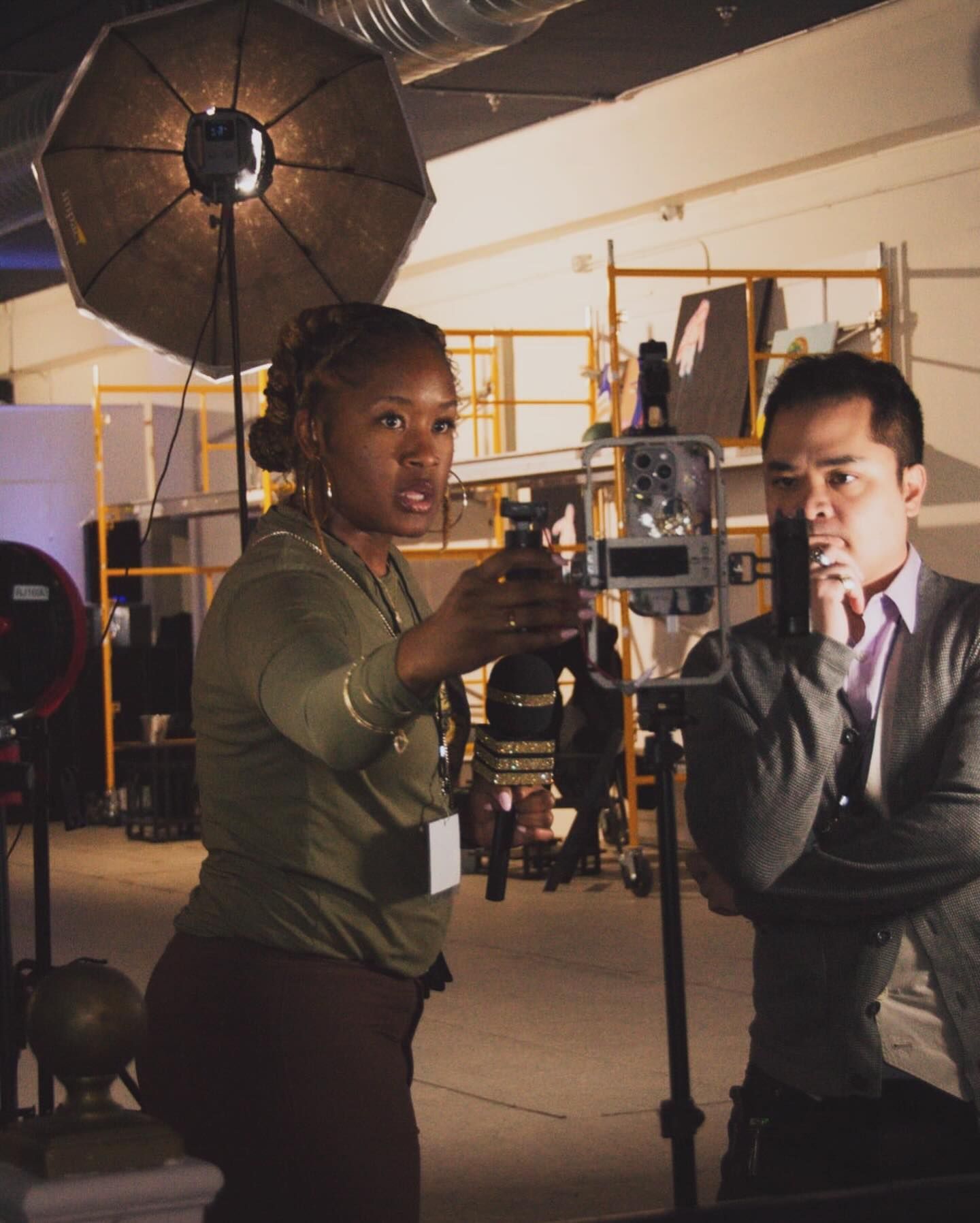 Two people collaborate during a professional photo shoot with studio lighting equipment and camera setup.