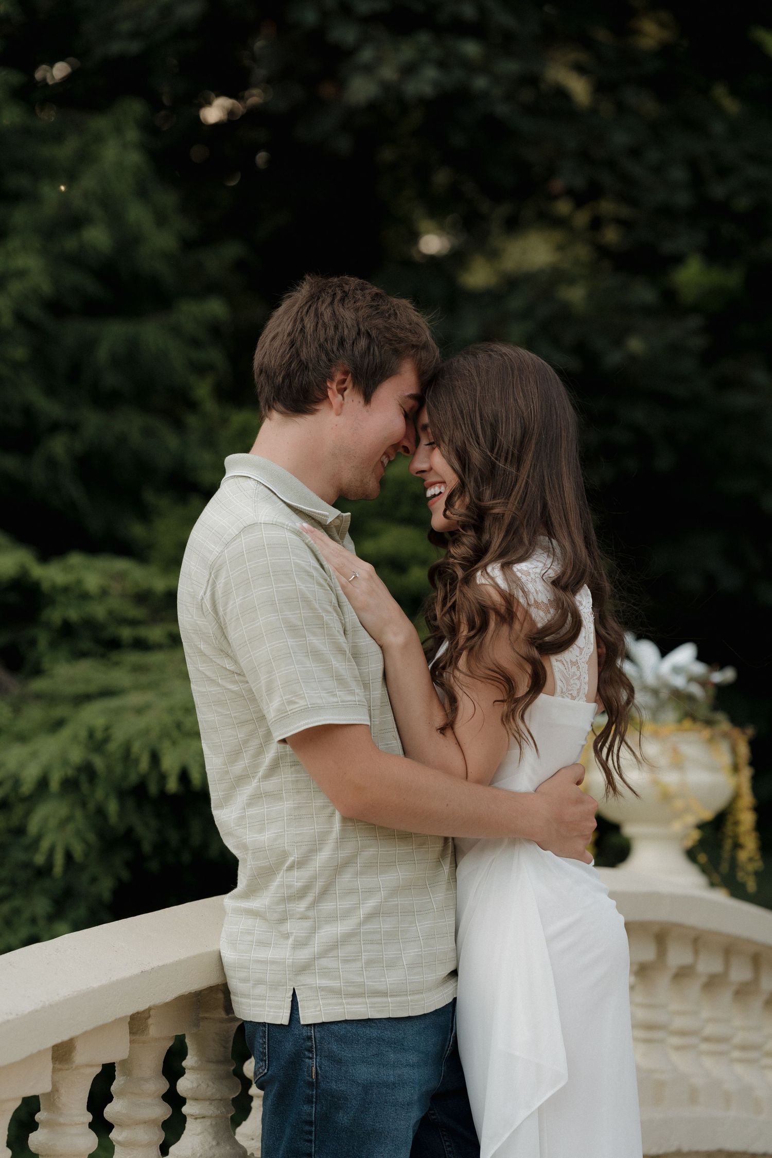 Happy couple laughing and embracing on a stone bridge surrounded by lush green trees in Halifax Public Gardens.