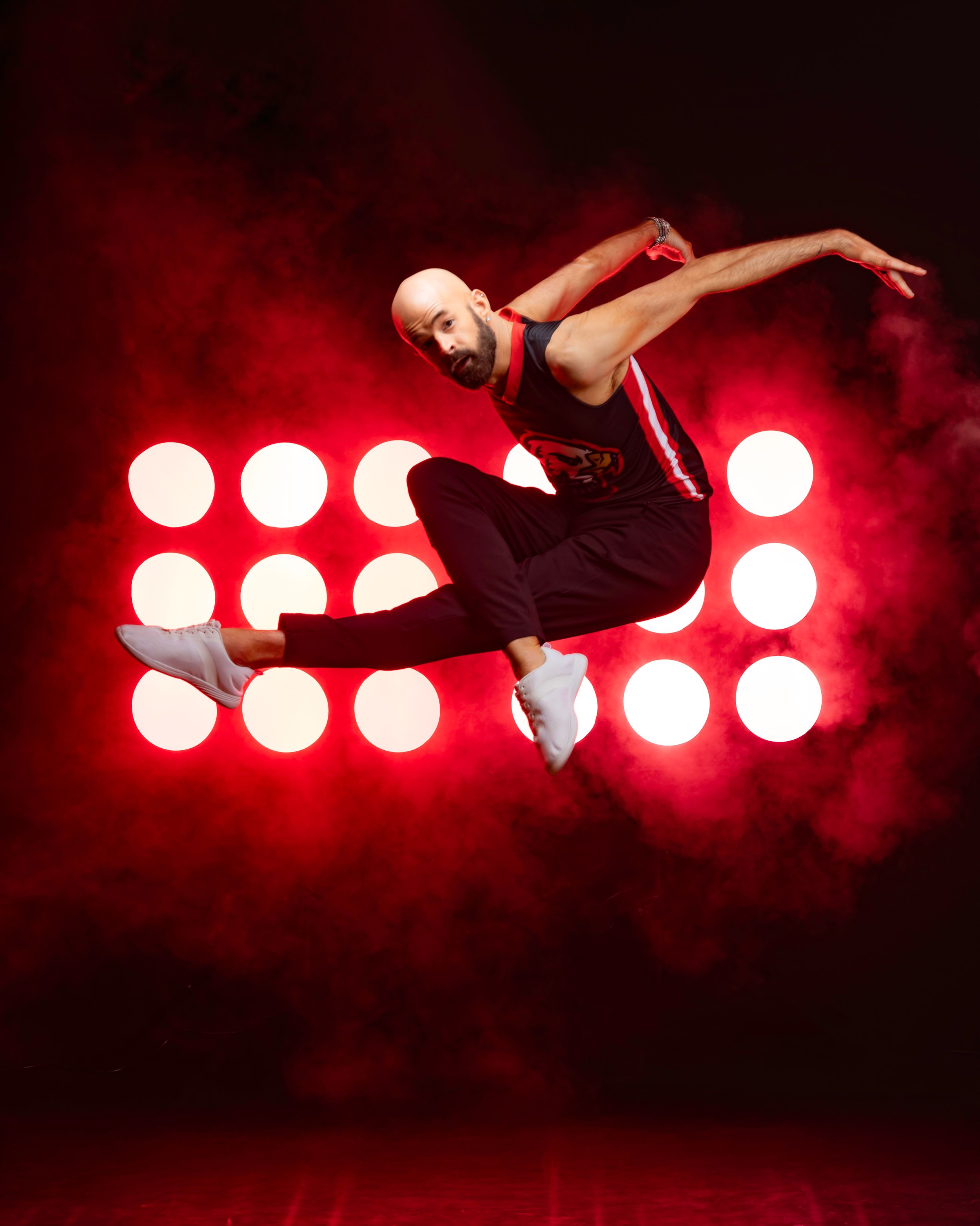 Dancer leaps gracefully through the air against dramatic red spotlights creating a dynamic silhouette effect.