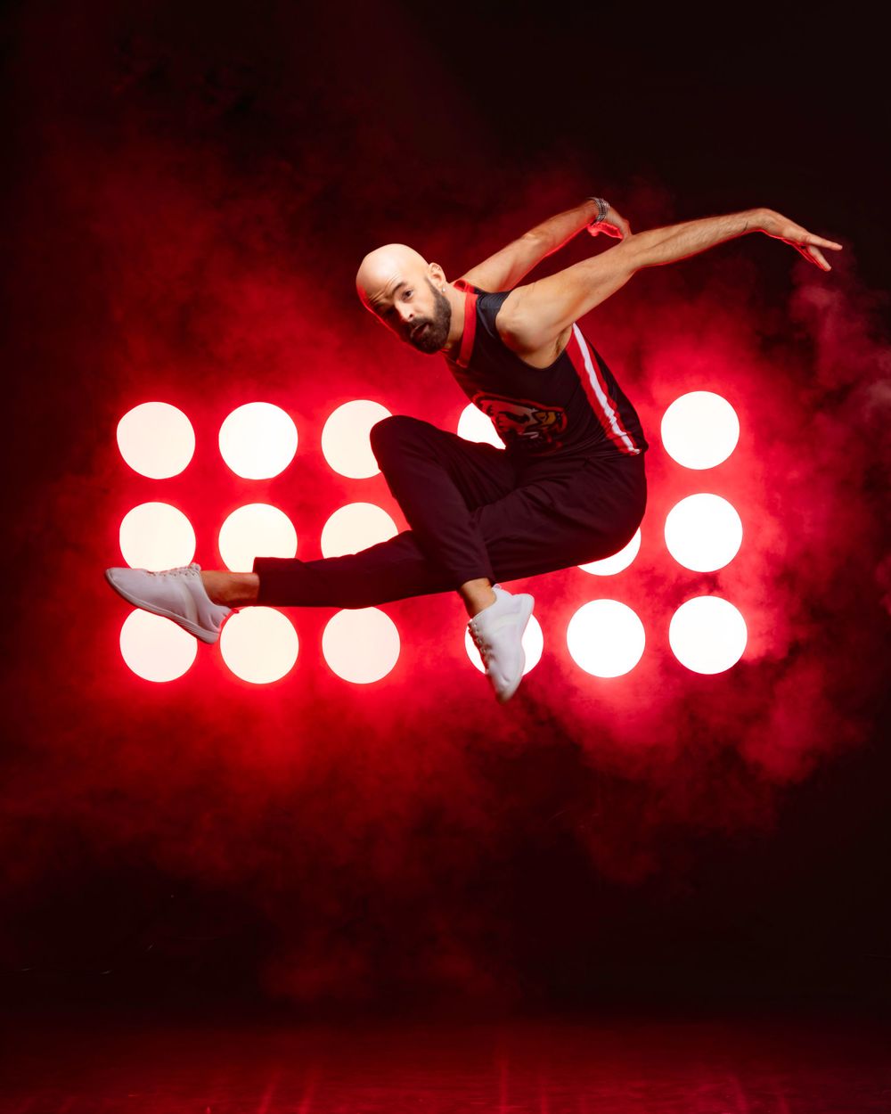 Dancer leaps gracefully through the air against dramatic red spotlights creating a dynamic silhouette effect.
