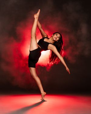 Portland Winterhawks Pro Dance Team Dancer in black performs a graceful high kick pose against a dramatic red and smoky background.