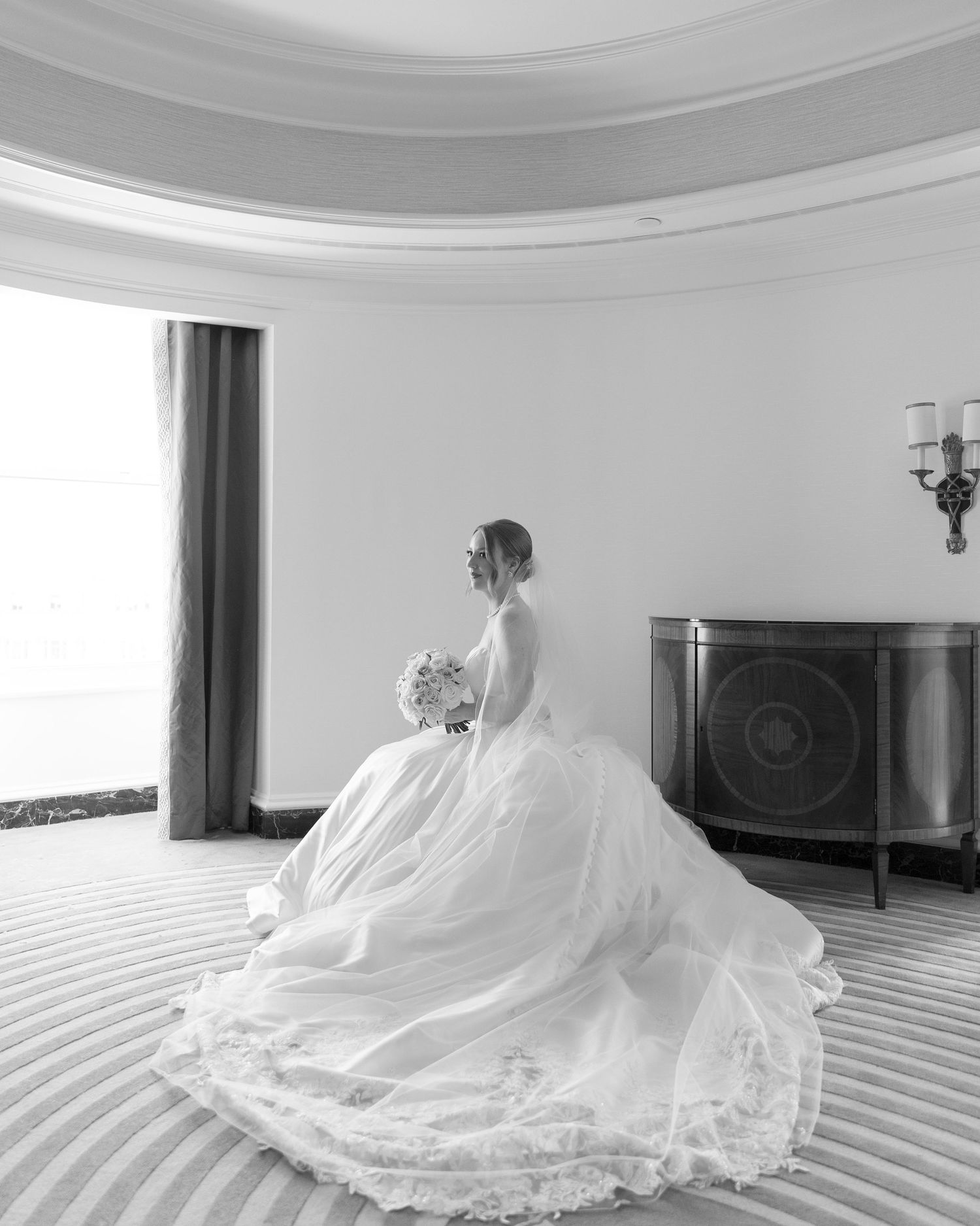 A bride in an elegant ball gown poses in a circular room with dramatic lighting.