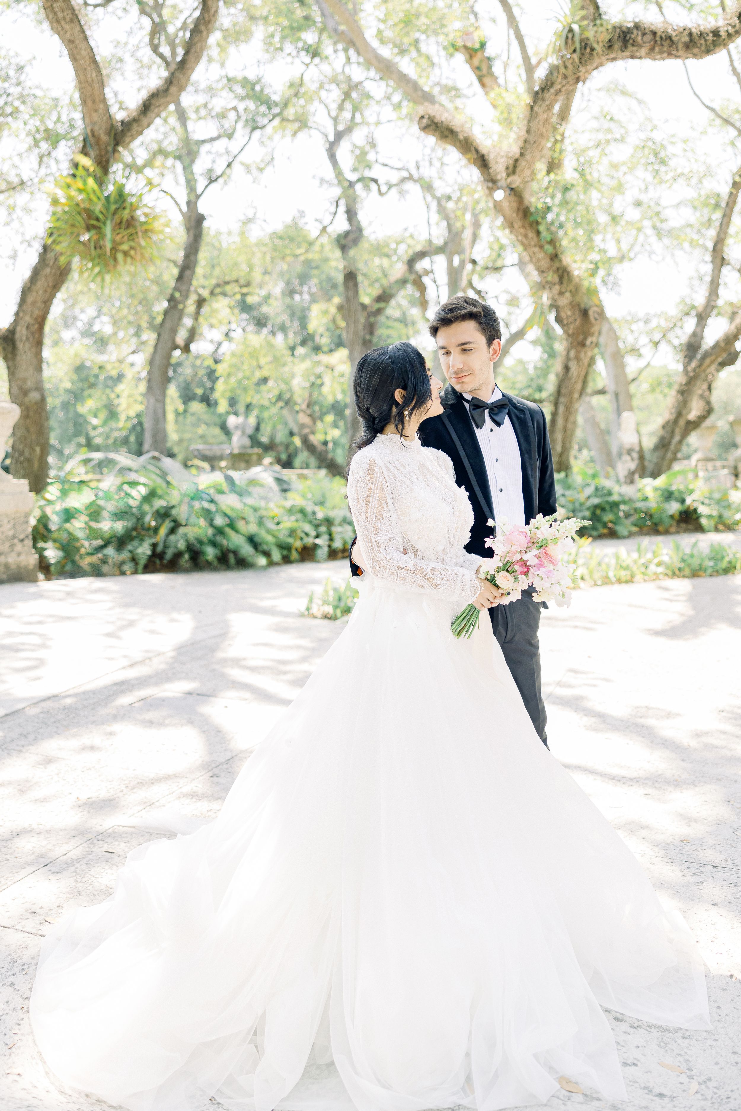 Romantic wedding couple share a moment in a sunlit garden with blooming trees.