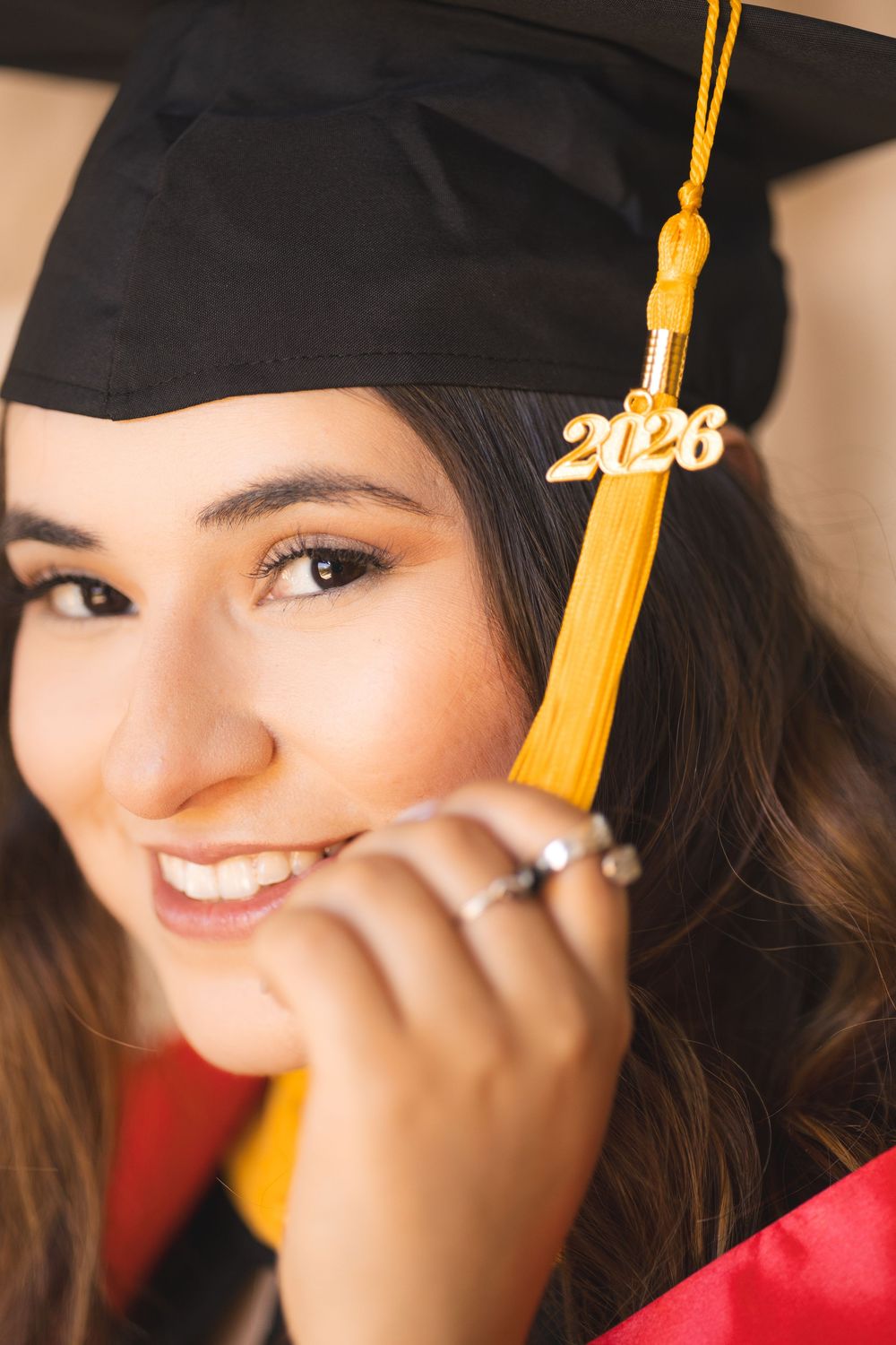 Smiling young woman in black graduation cap with gold 2026 tassel, wearing red graduation gown.