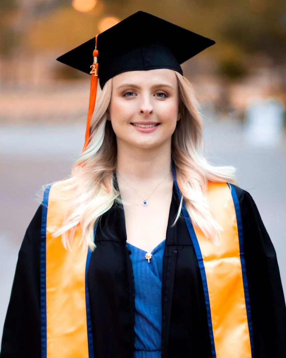Smiling female graduate in black cap and gown with gold sash posing for graduation portrait photo.