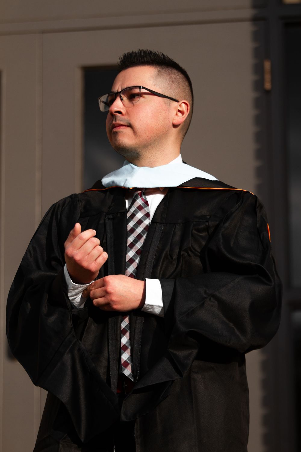 Man in black graduation gown and glasses adjusting his academic regalia during commencement ceremony.