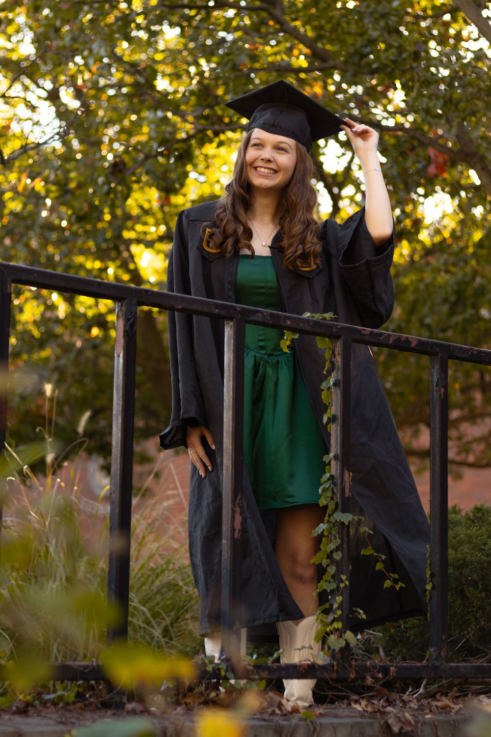 A graduation portrait of a young woman in her cap and gown smiling and holding the corner her cap.