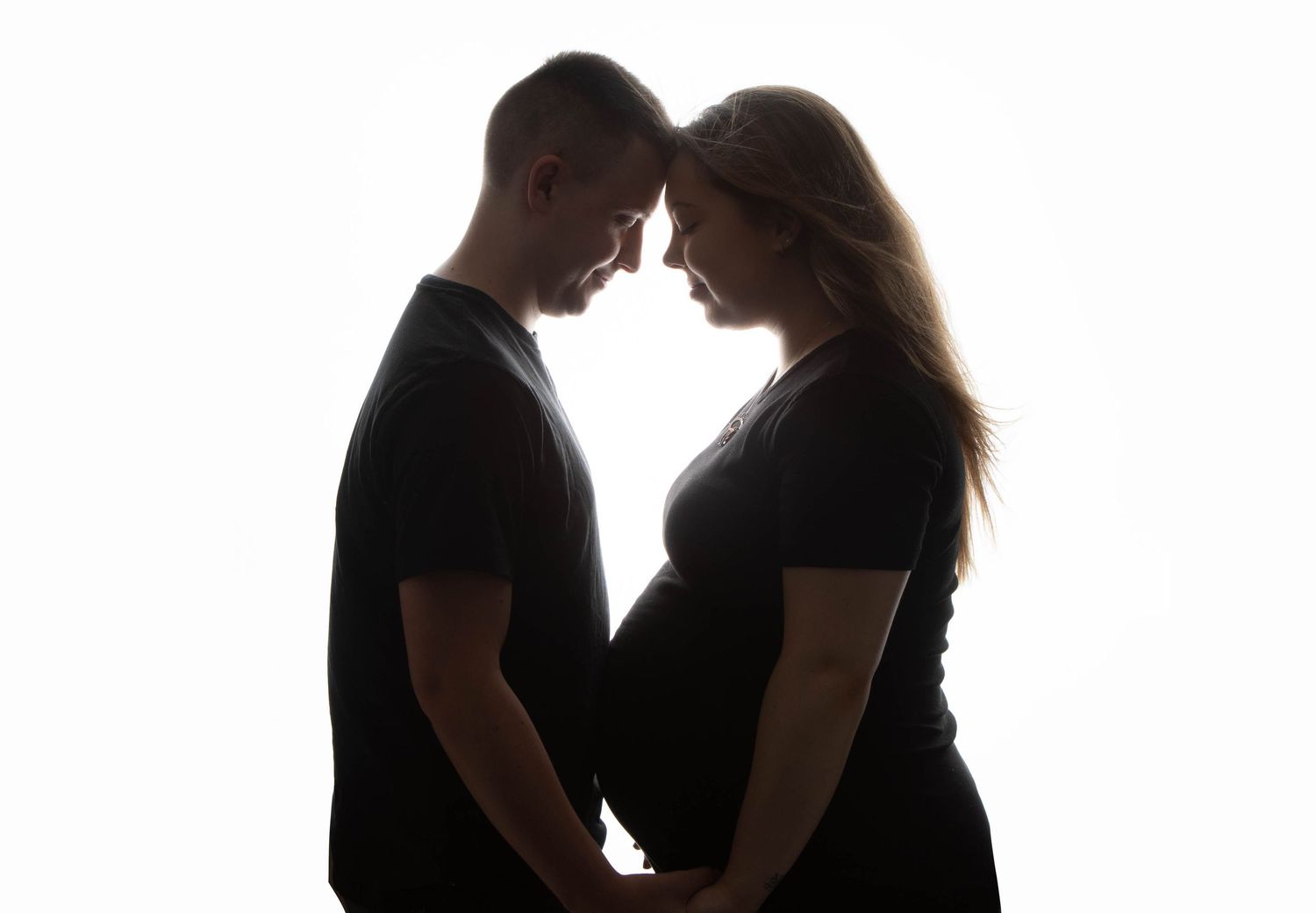 Romantic silhouette of couple touching foreheads while holding pregnant belly together.