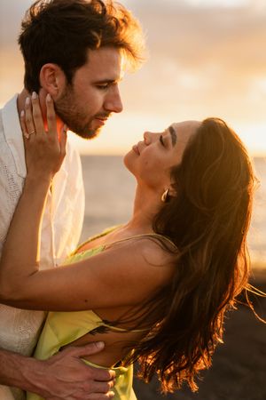 Romantic couple embracing at sunset on a beach, golden hour light glowing behind them.