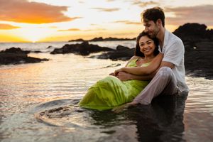 Couple sitting together in ocean tide pools at sunset, woman in green dress, romantic beach photography.