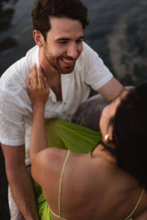 A smiling man in a white shirt gazes at a woman in a green dress during a romantic outdoor couples session.