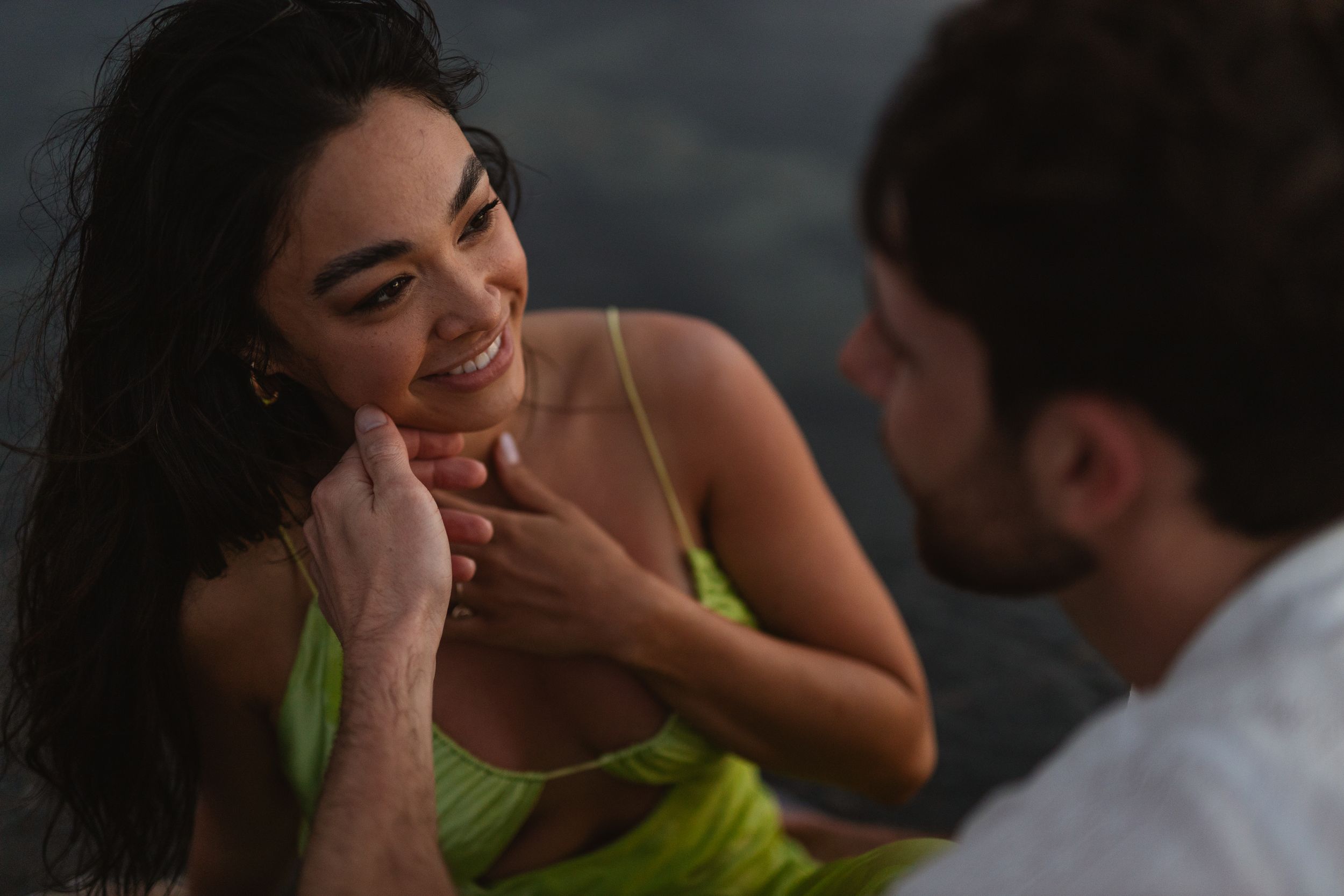 Romantic couple sharing a tender moment outdoors, woman in green dress smiling as man gently touches her face.