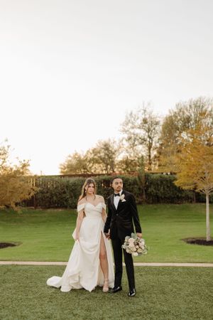 A couple poses together on a grassy lawn at golden hour with autumn trees in the background.
