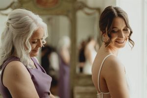 Two women share a joyful moment at a formal event, one wearing lavender and the other in a formal white dress.