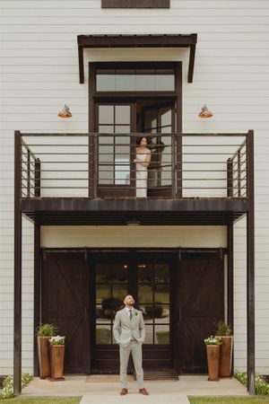 Modern farmhouse exterior featuring dark brown barn doors, horizontal railing balcony, and copper pendant lights.