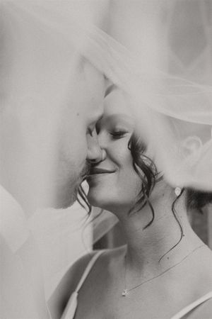 An artistic black and white photo showing a bride under her wedding veil with a gentle smile.