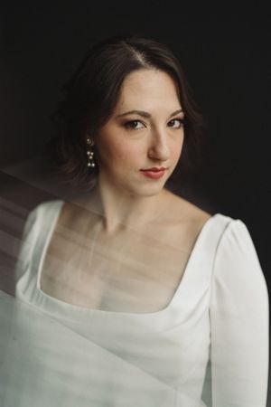 Elegant bridal portrait featuring a white square-neck long sleeve dress and delicate jewelry against a dark background.