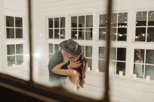 A romantic silhouette of a couple sharing an intimate kiss by large white windows in warm lighting.