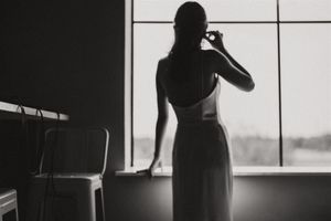 Silhouette of a woman in a dress standing by a window in black and white photography.