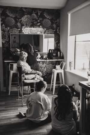 Black and white photo showing a cozy interior with children sitting on the floor and floral wallpaper in the background.