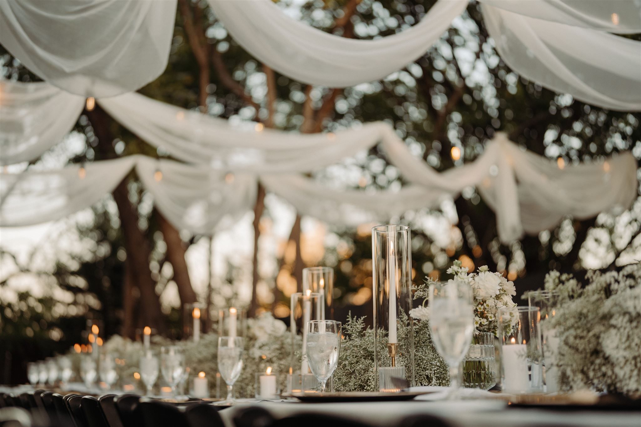 Elegant wedding reception table setting with white draping, candles and floral arrangements creating a romantic atmosphere.