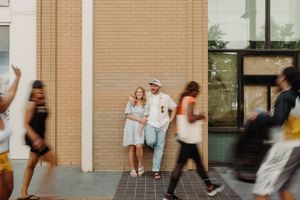 Dynamic street scene with motion blur of people walking past a brick and glass building.