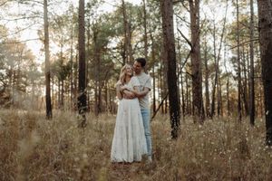 A romantic moment captured in a sunlit forest with tall pine trees and dry grass.