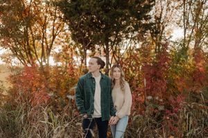 Couple enjoying autumn foliage in a park with golden sunset light glowing through red and orange trees.